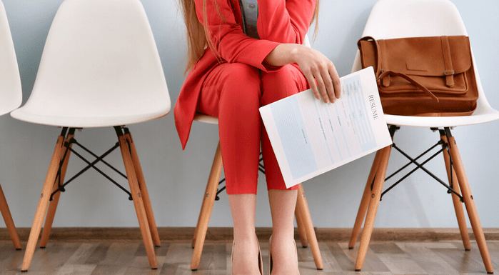 A woman sitting on a chair, holding a resume in her hand.