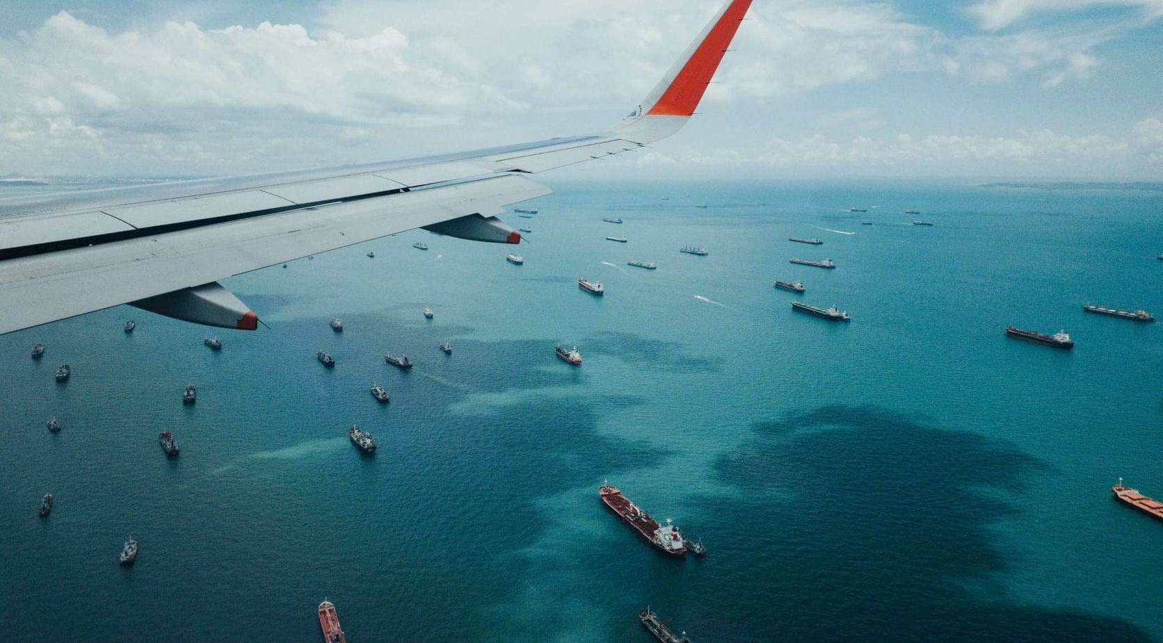 Airplane wing over sea with container ships