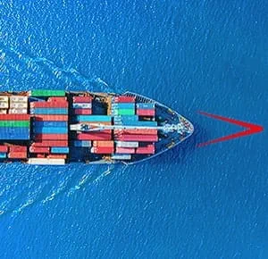 A cargo ship sailing on deep blue water, viewed from above. The vessel is loaded with colourful shipping containers arranged in neat rows, creating a striking contrast against the surrounding ocean.