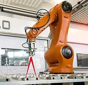 An industrial robotic arm in bright orange colour positioned over a metal work surface, equipped with a precision gripper tool. The setting is a modern manufacturing or assembly facility, with machinery and structural elements visible in the background.