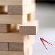 A wooden block tower game with one rectangular block partially pulled out from the stack, highlighting a moment of tension or strategy in gameplay. The blocks are light-coloured and arranged in alternating layers on a smooth surface.