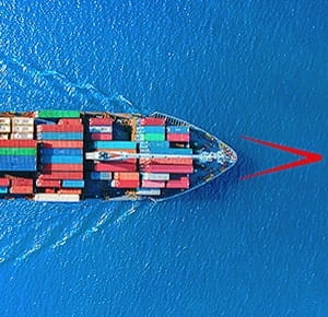 A cargo ship sailing on deep blue water, viewed from above. The vessel is loaded with colourful shipping containers arranged in neat rows, creating a striking contrast against the surrounding ocean.