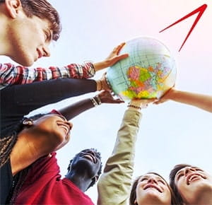 A group of people standing in a circle outdoors, raising a colourful globe together toward the sky. The background shows a bright, clear sky, symbolizing global unity, teamwork, and diversity.