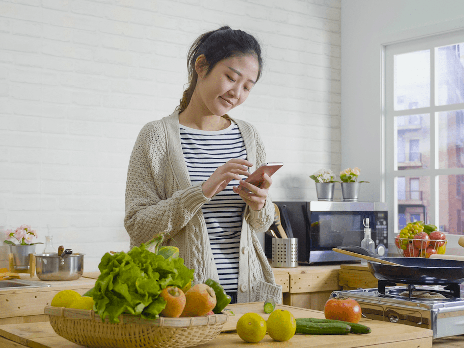 Young woman looking at her mobile phone whilst preparing food in her kitchen