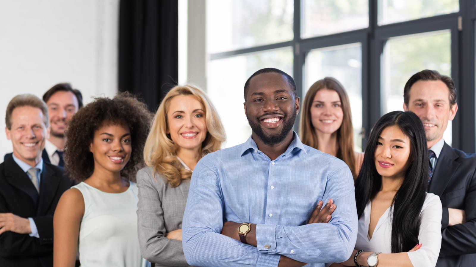 A diverse group of professionals standing together in a modern office, facing the camera with arms crossed