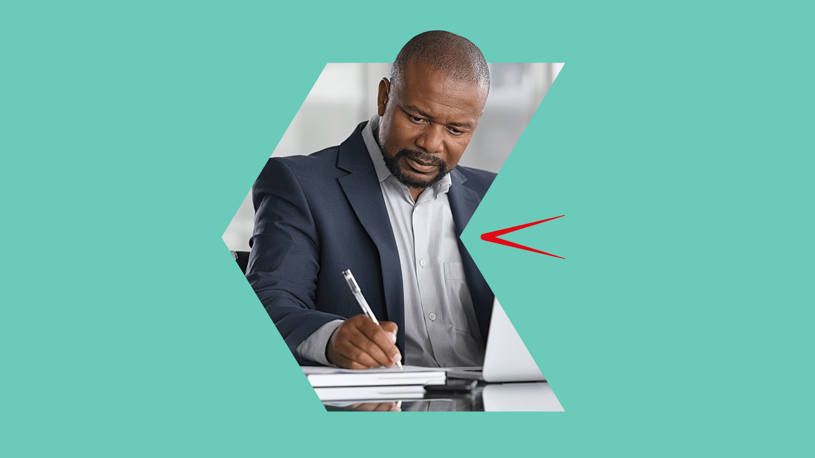 A man in a suit writing notes beside a laptop