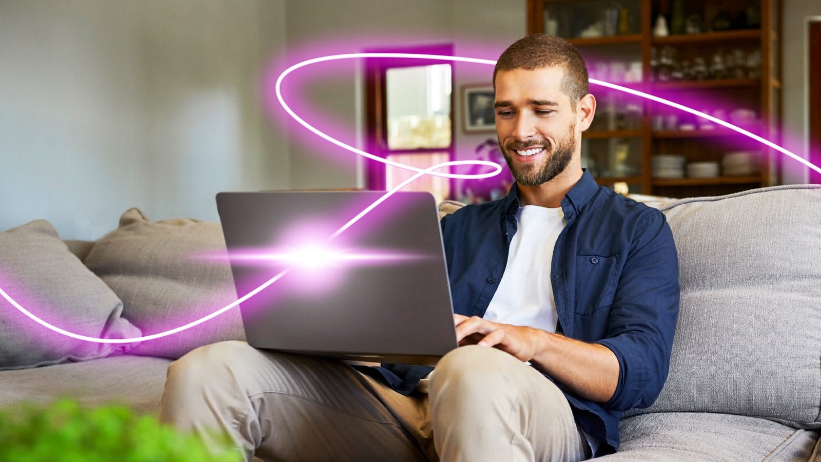 A man sitting on a grey sofa using a laptop, with a digitally added glowing pink light trail swirling around them.