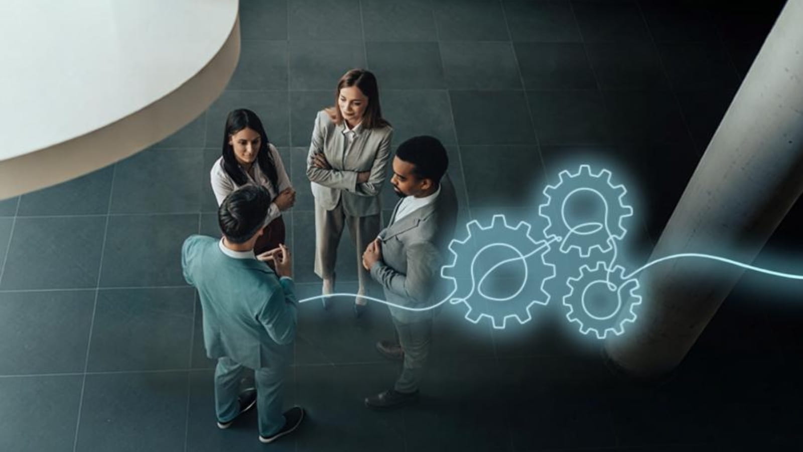 Four people standing in a circle indoors, with a glowing graphic of interlocking gears beside them.