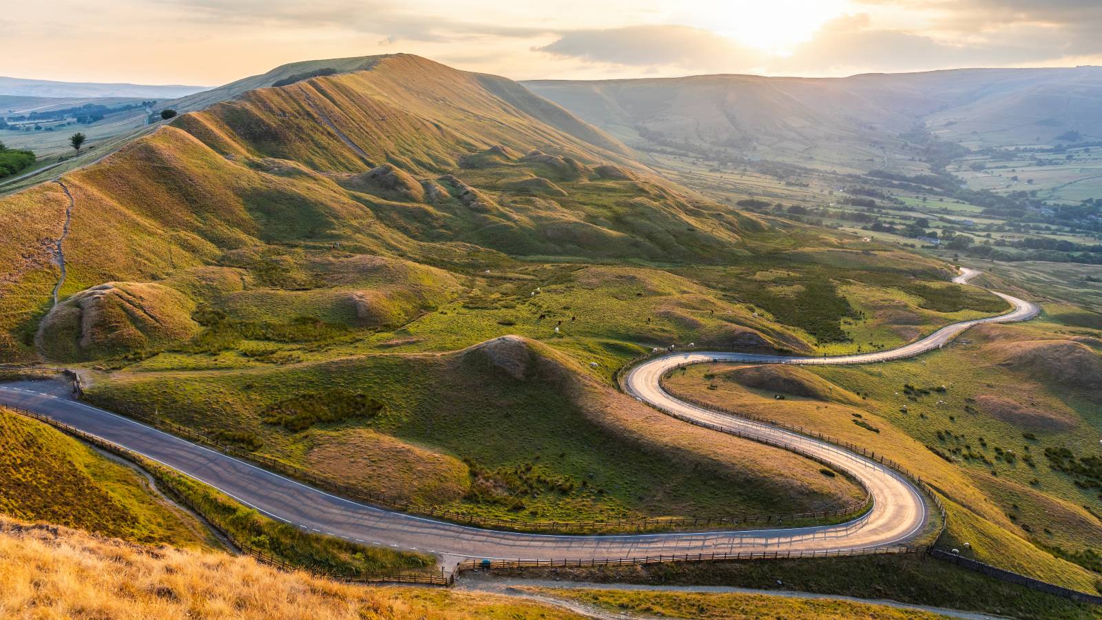 Road winding through hilly countryside with sun rising in the background