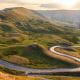 Road winding through hilly countryside with sun rising in the background