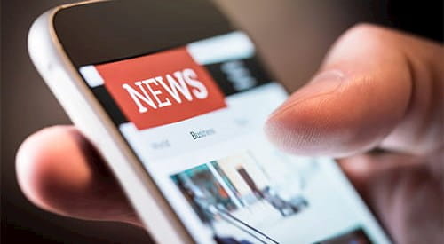 A hand holding a smartphone showing a news app