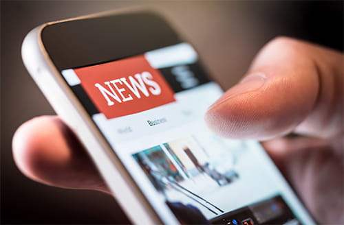 A hand holding a smartphone showing a news app