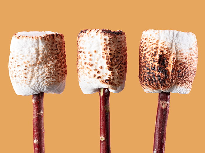 three toasted marshmallows on sticks orange background