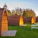 camping pods wood shingles arched rooves grounds green grass picnic benches blue sky