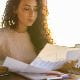 young woman curly dark long hair looking at paperwork charts graphs data sun shine behind through window