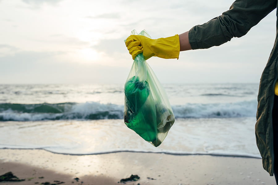 A person wearing rubber gloves standing on a beach holding a bag of rubbish