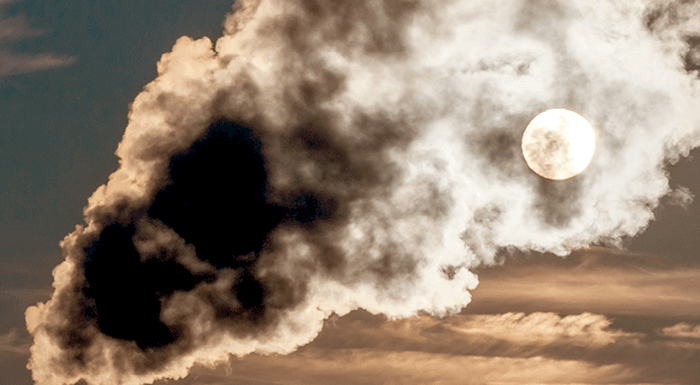 The moon seen through smoke coming from a smokestack