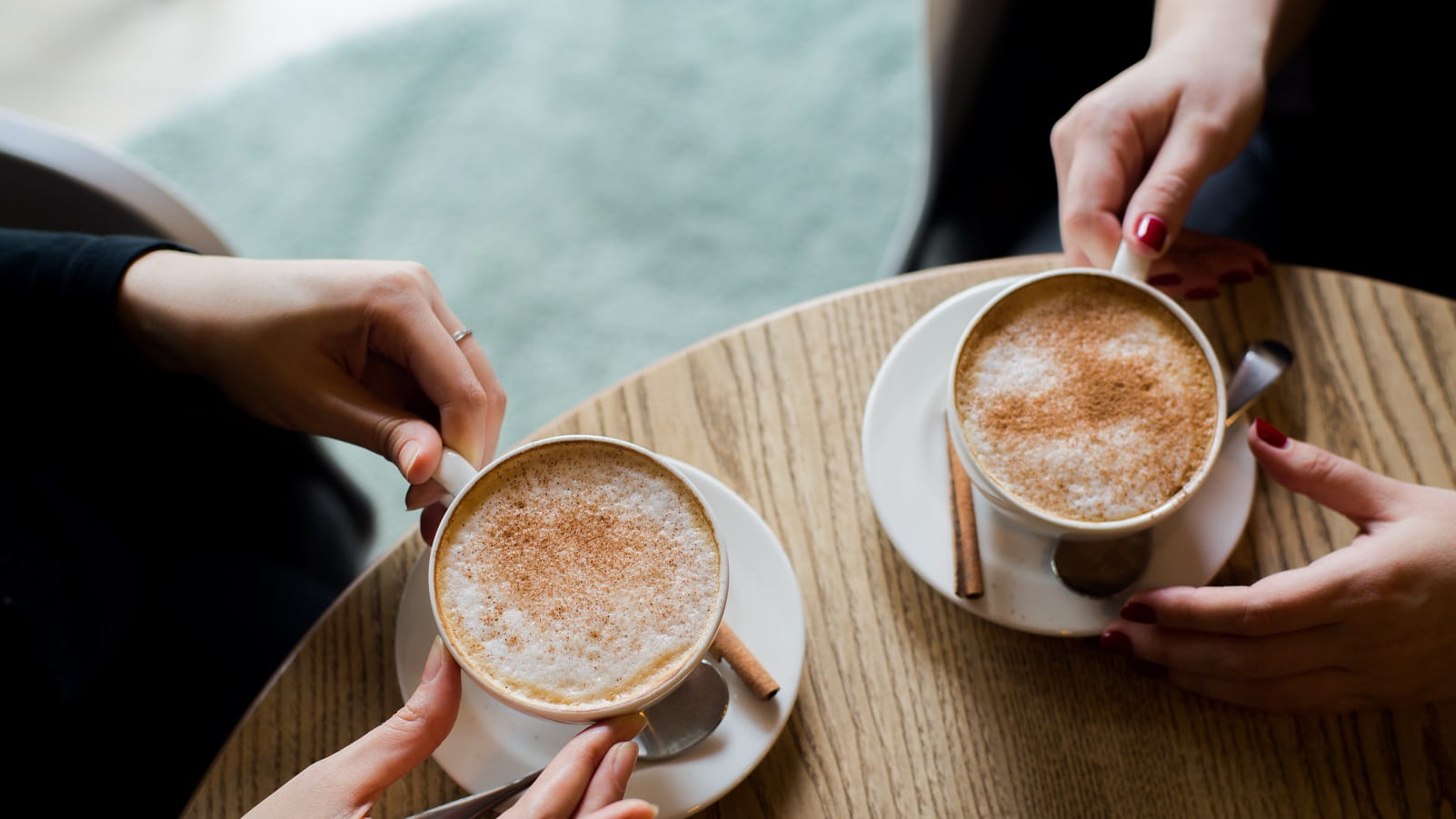 Two cups of coffee on a table with hands holding them