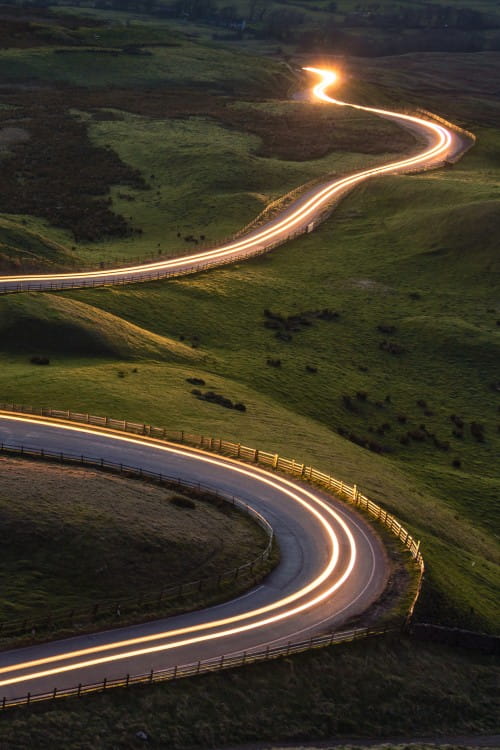 Road winding through hilly countryside with sun rising in the background