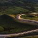 Road winding through hilly countryside at dusk with car lights blurred on road.