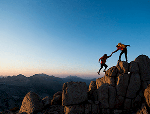 Two people scaling a peak, one helping the other up