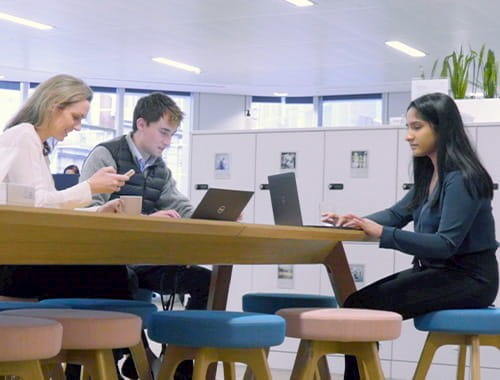 apprentices colleagues sitting at a table desk in an office with lockers and plants