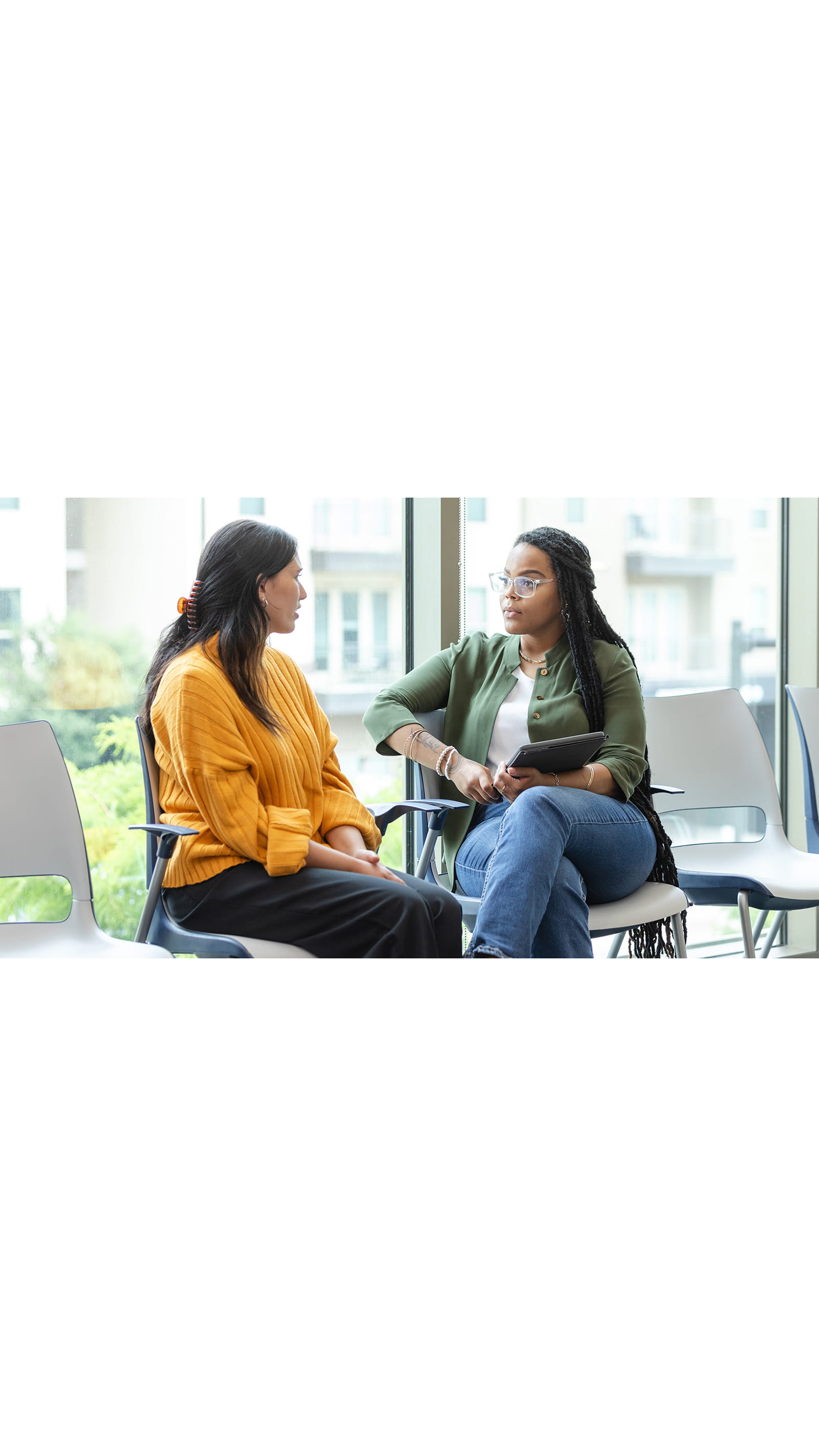 two women colleagues businesswomen having a difficult conversation in an office meeting room sat on white chairs in front of windows