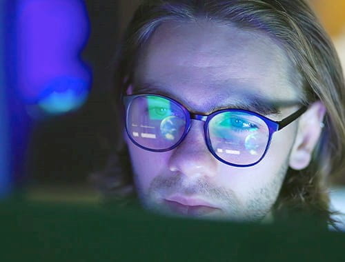 young man glasses reflecting computer screen dark room office