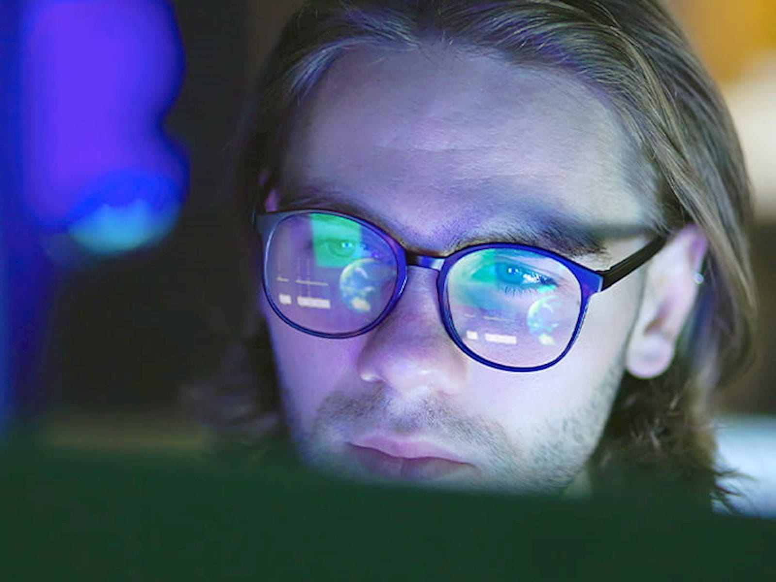 young man glasses reflecting computer screen dark room office