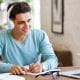 young man student studying looking at laptop wearing headphones writing taking notes