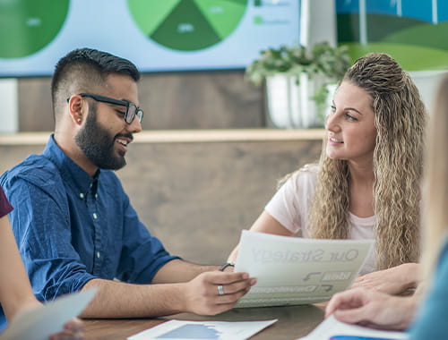 meeting office colleagues co-workers employees talking looking at paperwork charts graphs on screen