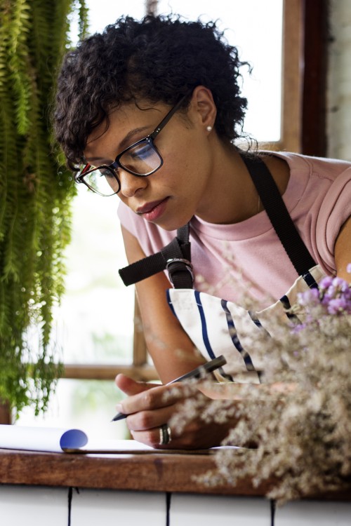 Woman working in a florist. She is completing paperwork at a desk, looking down at what she's writing.