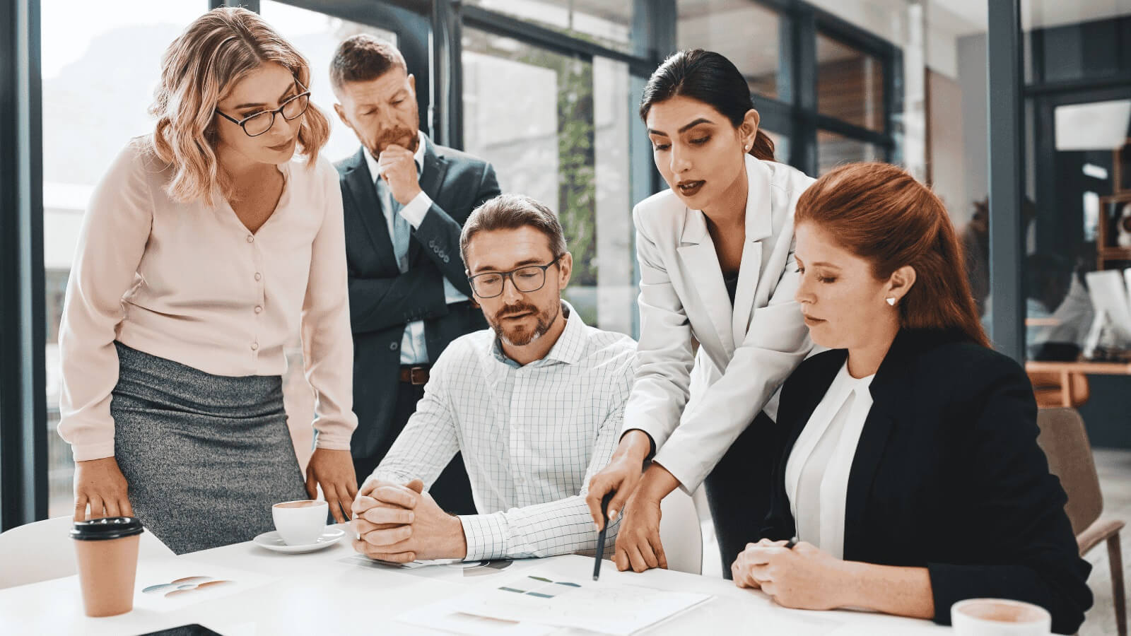 Five people in a team meeting, focused on a report laid out in front of them on the table