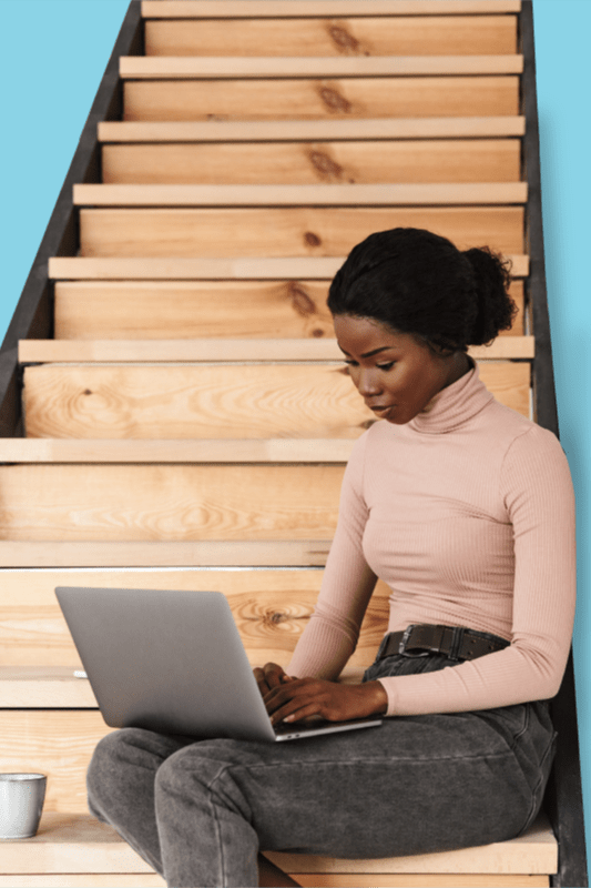 Image of woman sat on stairs working on laptop