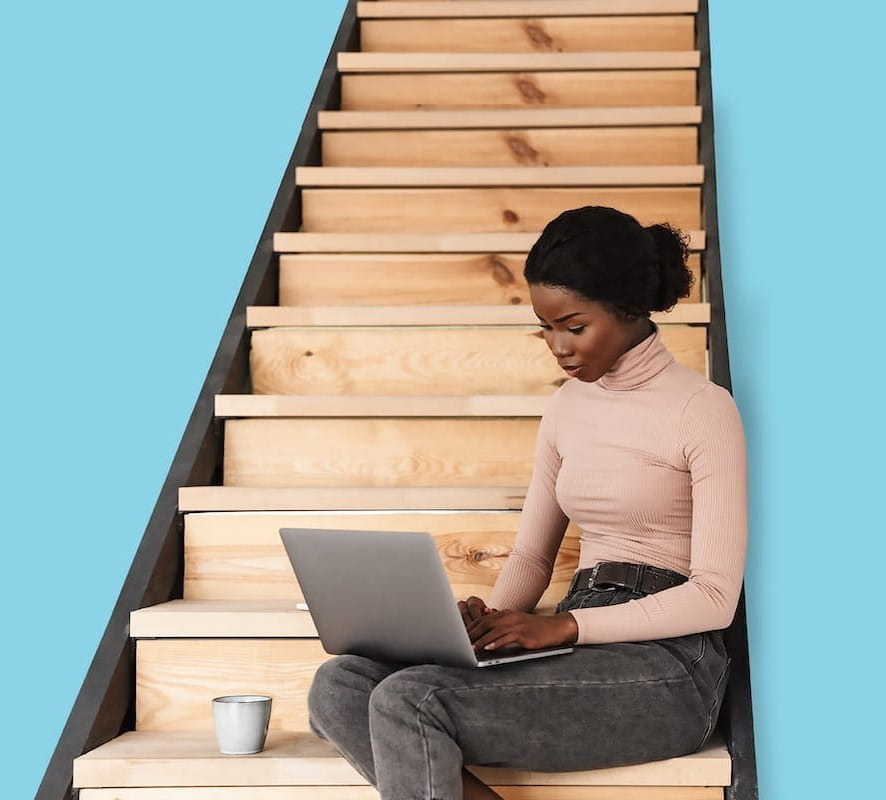 Image of woman sat on stairs working on laptop
