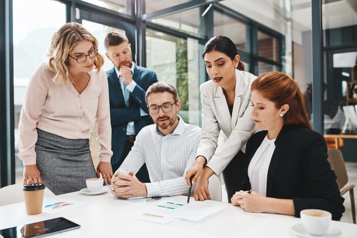 Five people in a team meeting, focused on a report laid out in front of them on the table