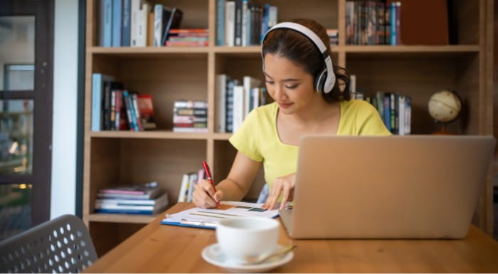 Person with headphones on with laptop taking notes