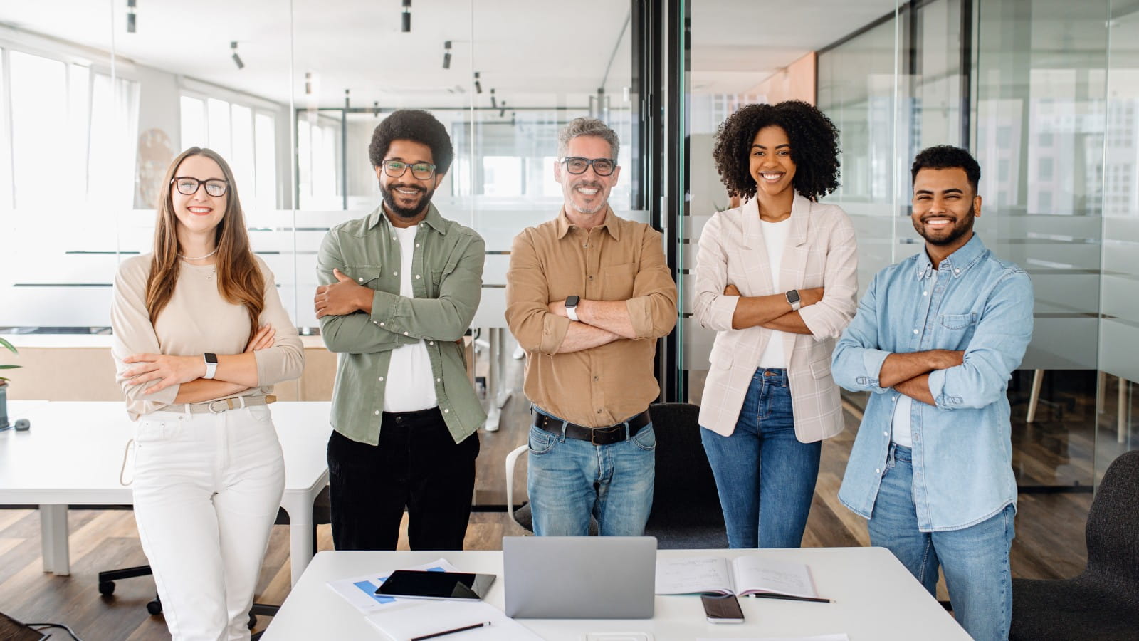 Diverse group of five colleagues stood behind a desk and smiling at the camera.
