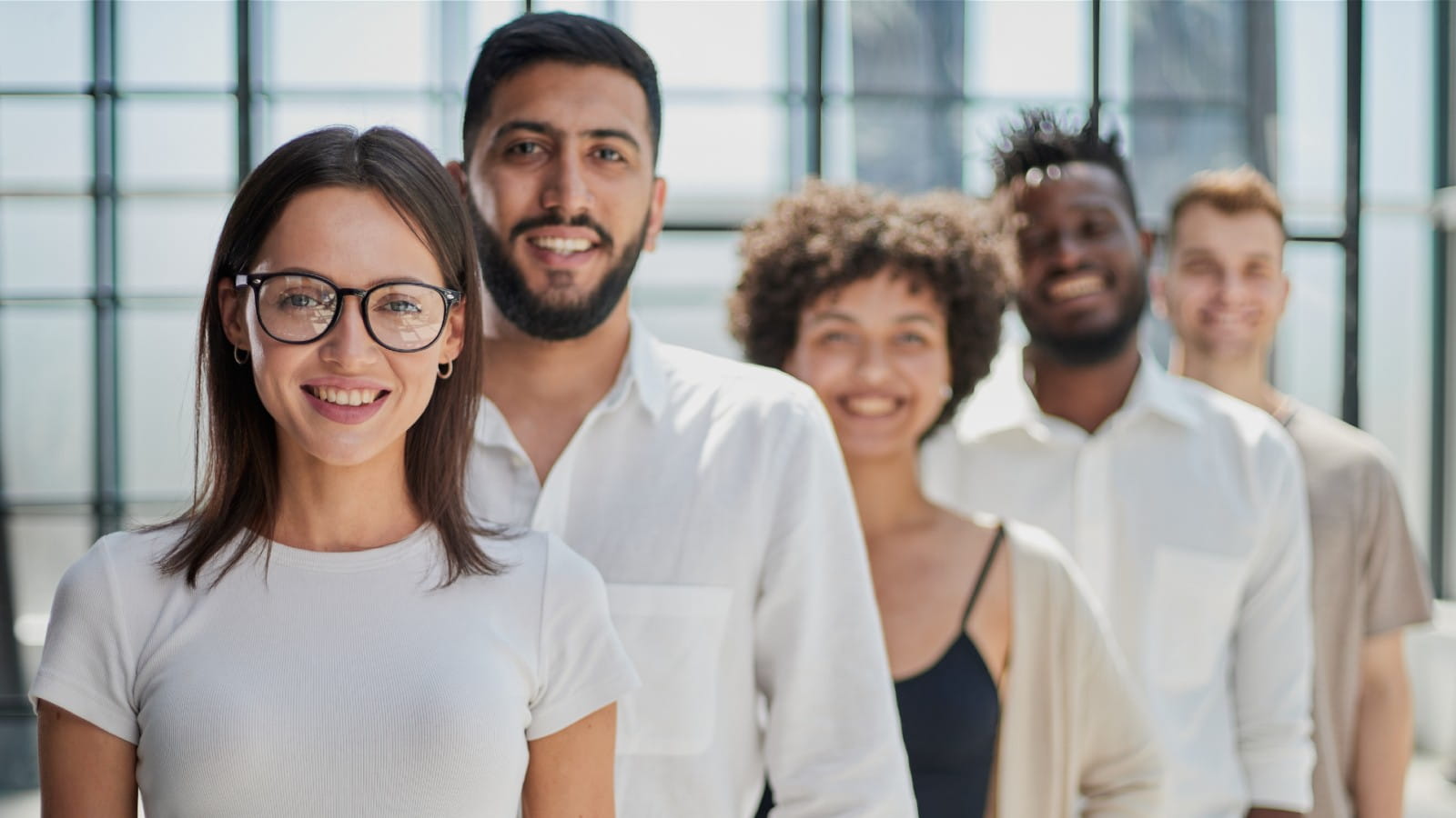 Diverse group of colleagues stood in a line outside their office, all are smiling at the camera.