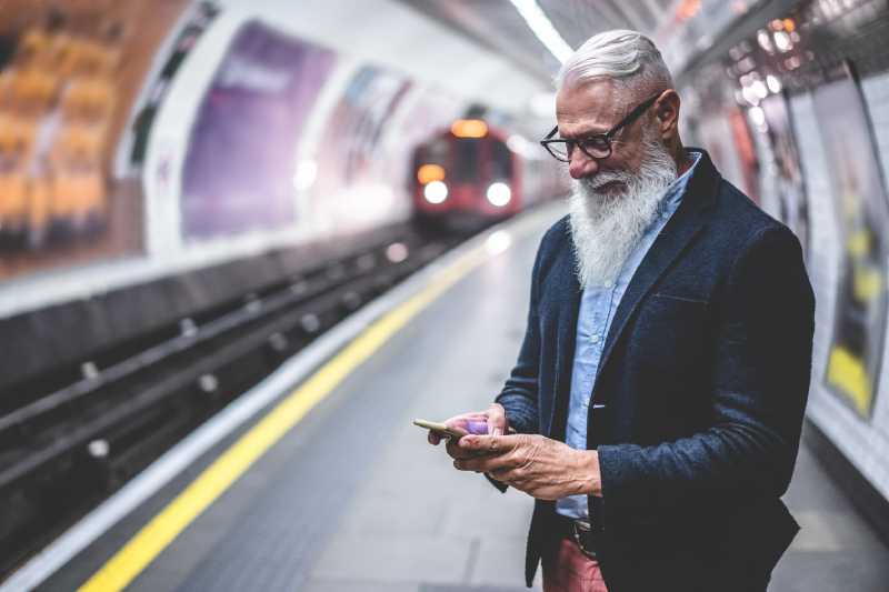 Mature man with grey beard checking phone at London Underground