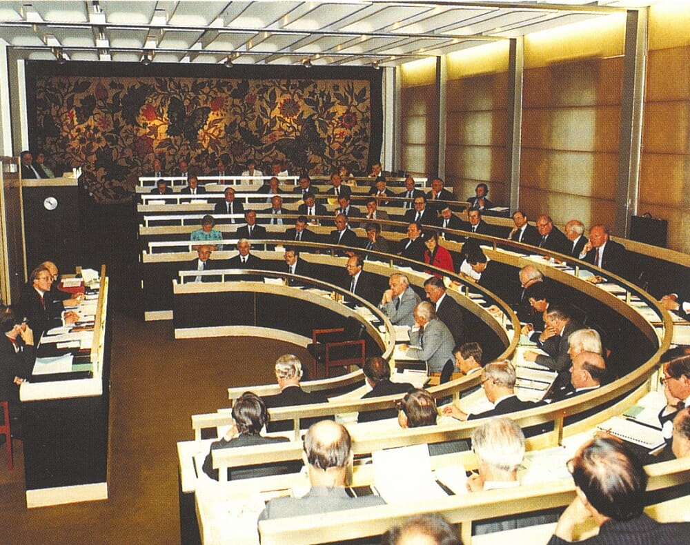 a small auditorium, in use by many people and a tapestry on the end wall