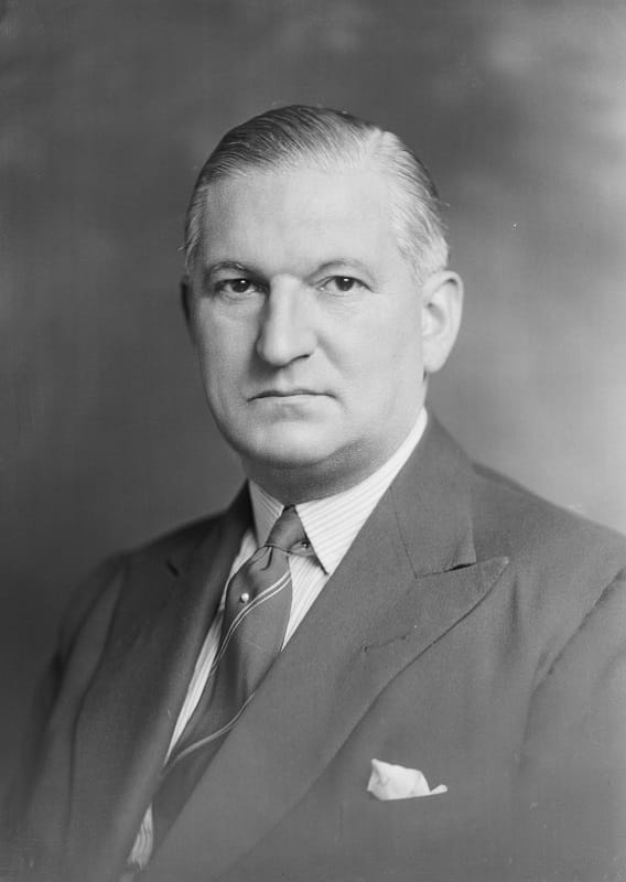 Head and shoulders shot of a stern looking man in 1940s jacket and tie
