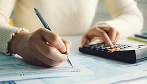 A person working at a desk with a calculator, pen and papers