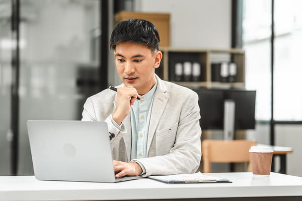 Male holding a pen, working on his laptop