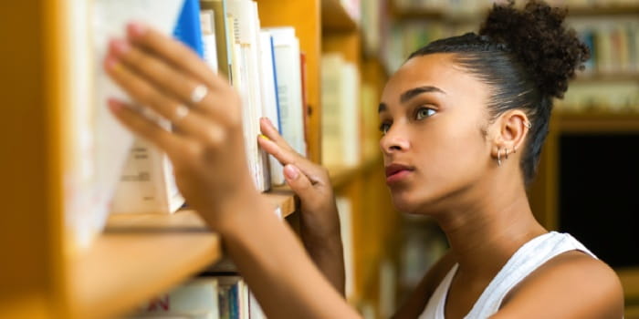 Young woman taking a book down from a library shelf