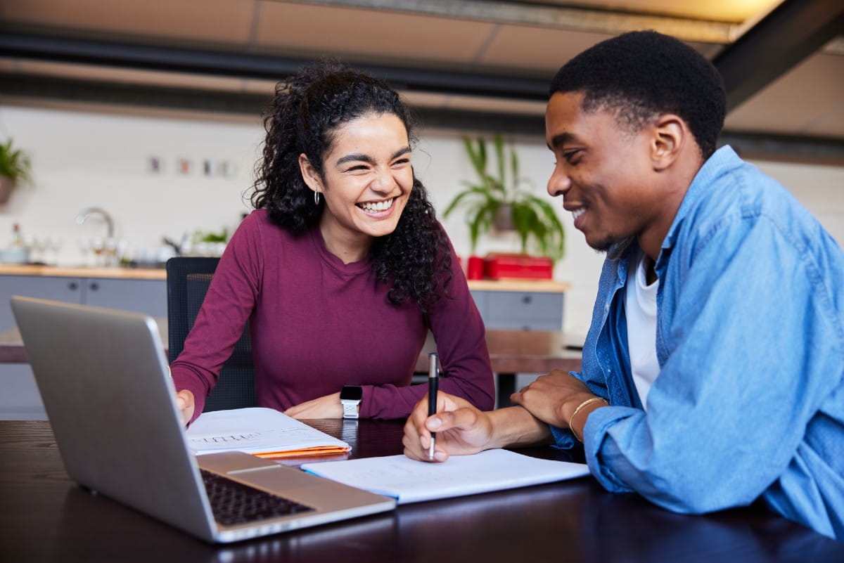 Image of two students smiling as they work together with notepads and a laptop