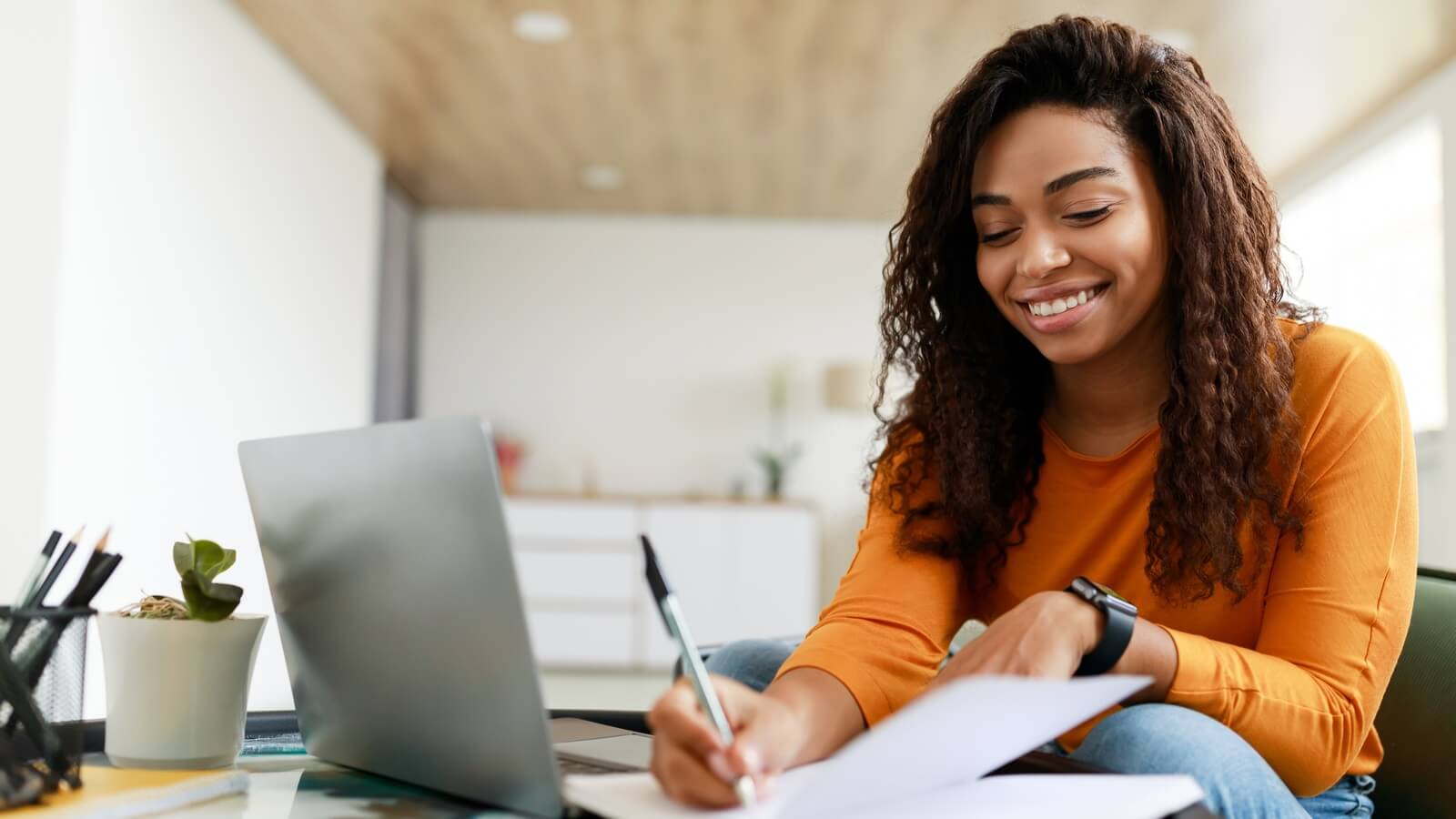 Smiling young woman sitting at desk, working on laptop
