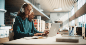 Young female student wearing headphones while working on her laptop at the library
