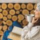 young woman knitted grey beanie hat cream jumper sweater mug hot drink book wood logs winter holiday