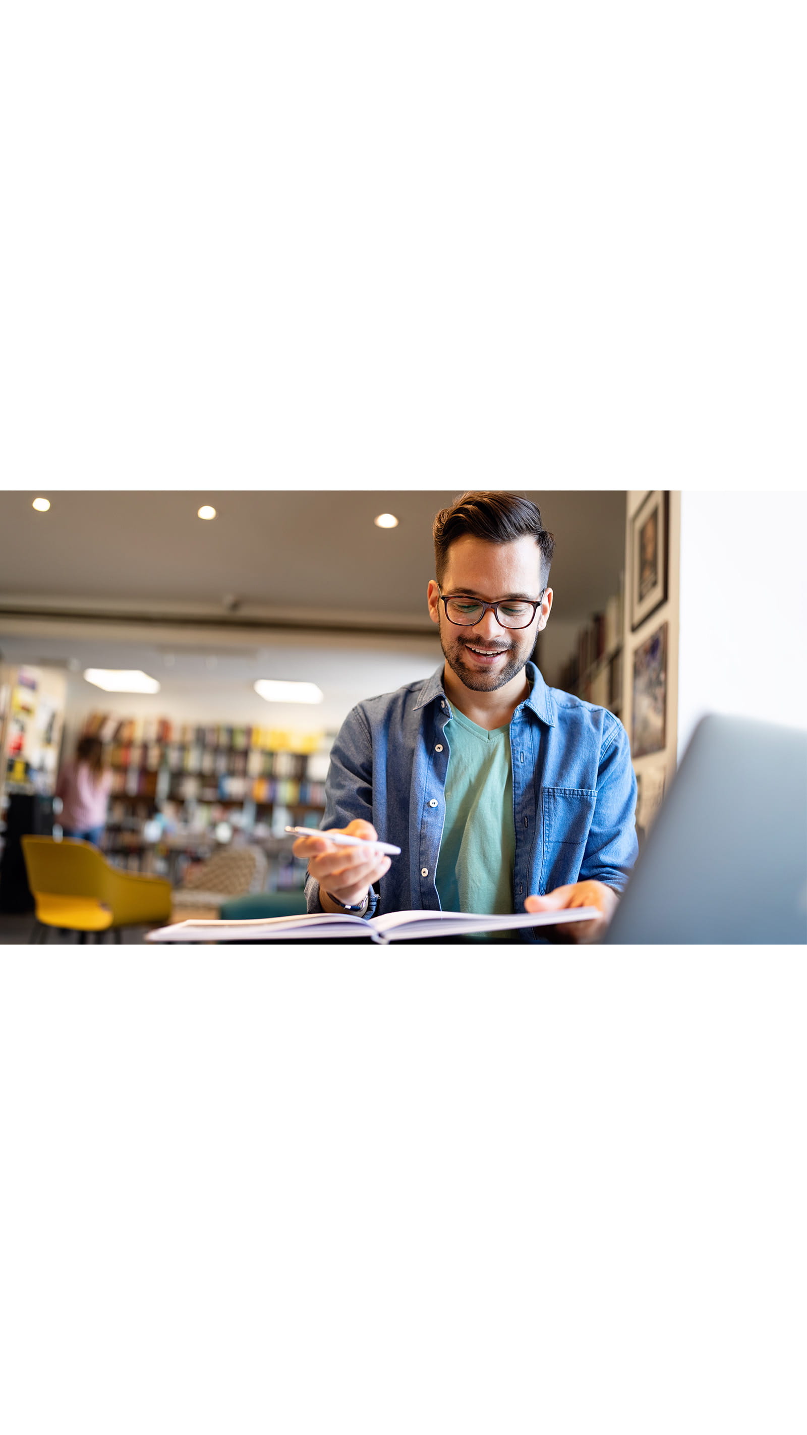 young man glasses student studying pen paper folder book denim shirt laptop office library